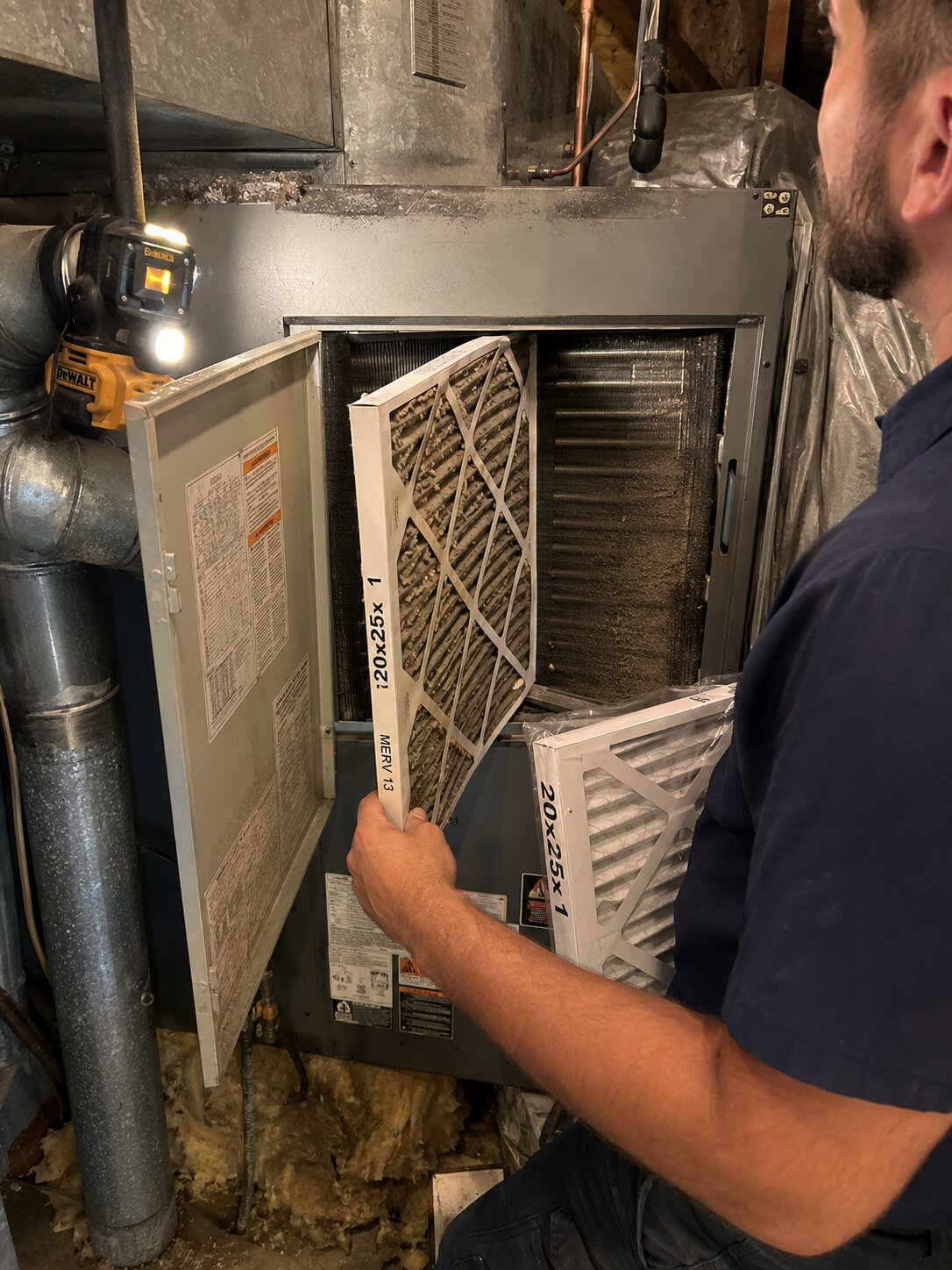 HVAC technician removing heavily loaded pleated filter from air handler cabinet during indoor air quality service