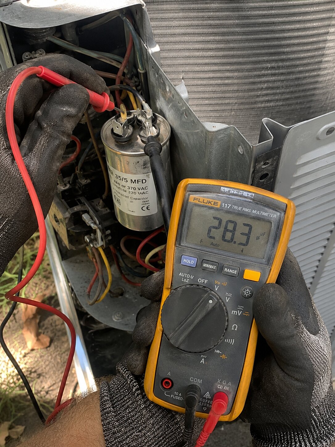 Technician measuring AC capacitor microfarads with multimeter showing reading below label rating