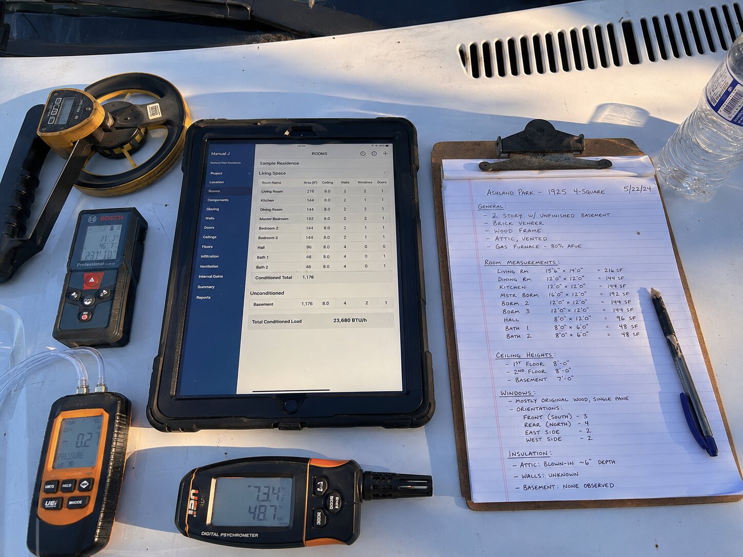 Manual J load calculation in progress on tablet with handwritten assessment notes and measurement tools on service van hood